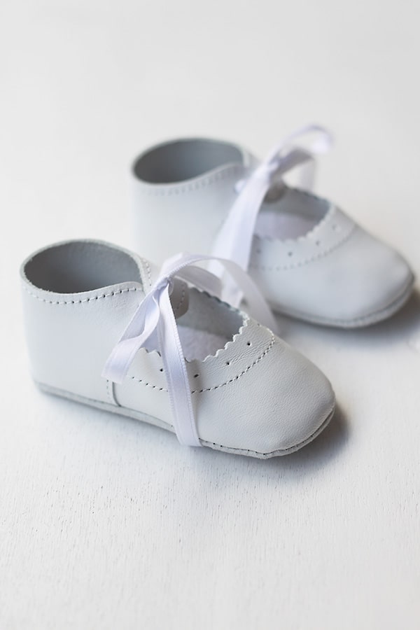 Chaussons ballerines bébé fille en cuir blanc pour cérémonie ou baptême. Se ferme en nouant un ruban de satin. Vue de côté.
