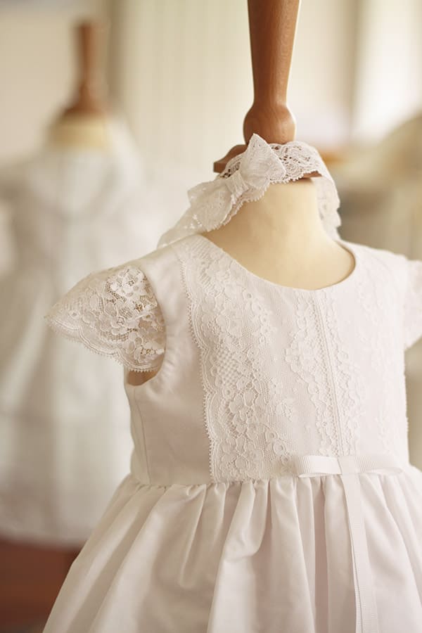 Bandeau cheveux bébé fille en dentelle blanche avec un nœud sur le côté. Idéal pour un baptême ou une cérémonie. Photo du bandeau porté avec une robe.