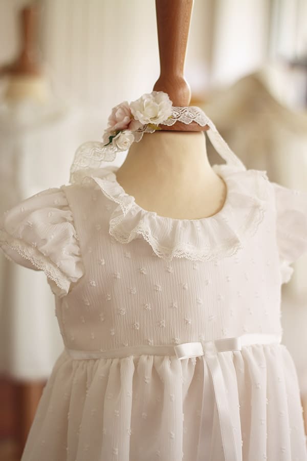 Bandeau cheveux bébé fille en dentelle blanc cassé avec fleurs blanches et roses. A porter pour un baptême ou une cérémonie. Photo du bandeau porté avec une robe.