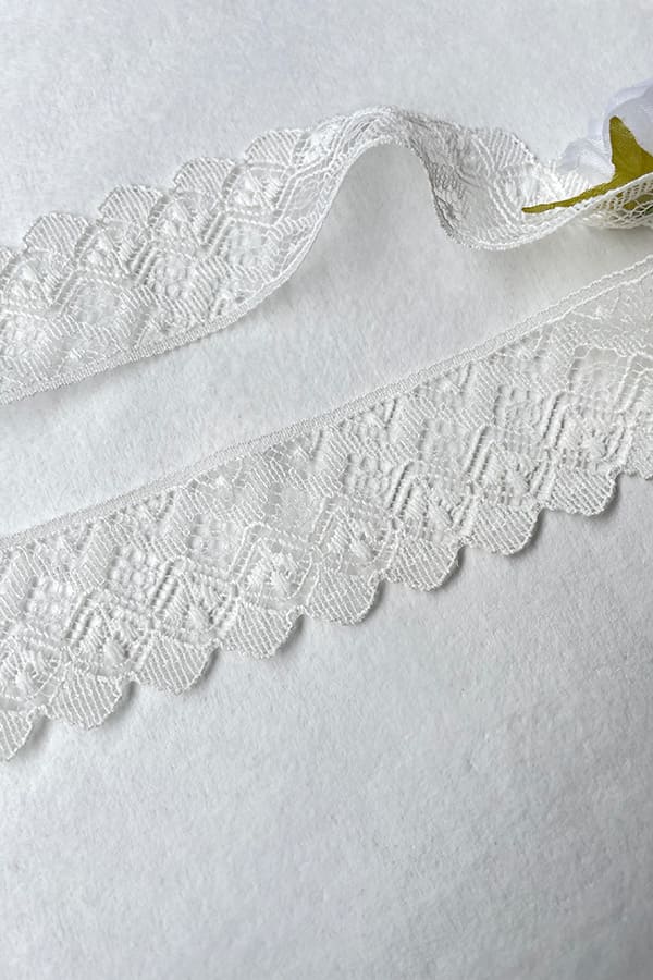Bandeau cheveux bébé fille en dentelle blanc cassé avec fleurs blanches et roses. A porter pour un baptême ou une cérémonie. Photo du gros plan de la dentelle.