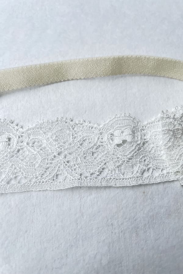 Bandeau cheveux bébé fille en dentelle blanc cassé avec nœud sur le côté. A porter pour un baptême ou une cérémonie. Photo u gros plan de la dentelle.