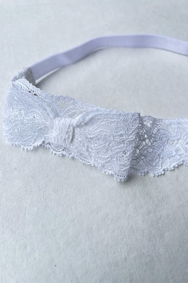 Bandeau cheveux bébé fille en dentelle blanche avec un nœud sur le côté. Idéal pour un baptême ou une cérémonie. Photo du nœud.