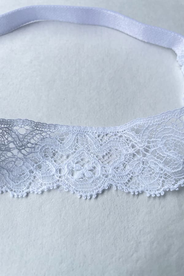 Bandeau cheveux bébé fille en dentelle blanche avec un nœud sur le côté. Idéal pour un baptême ou une cérémonie. Photo du gros plan de la dentelle.