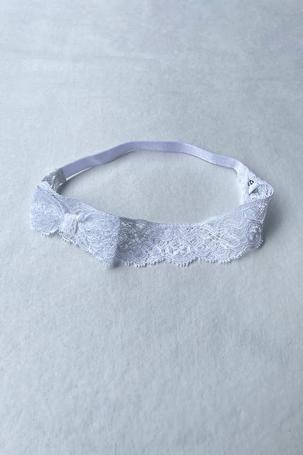 Bandeau cheveux bébé fille en dentelle blanche avec un nœud sur le côté. Idéal pour un baptême ou une cérémonie. Boutique Fil de Légende à Paris, Neuilly-sur-Seine.