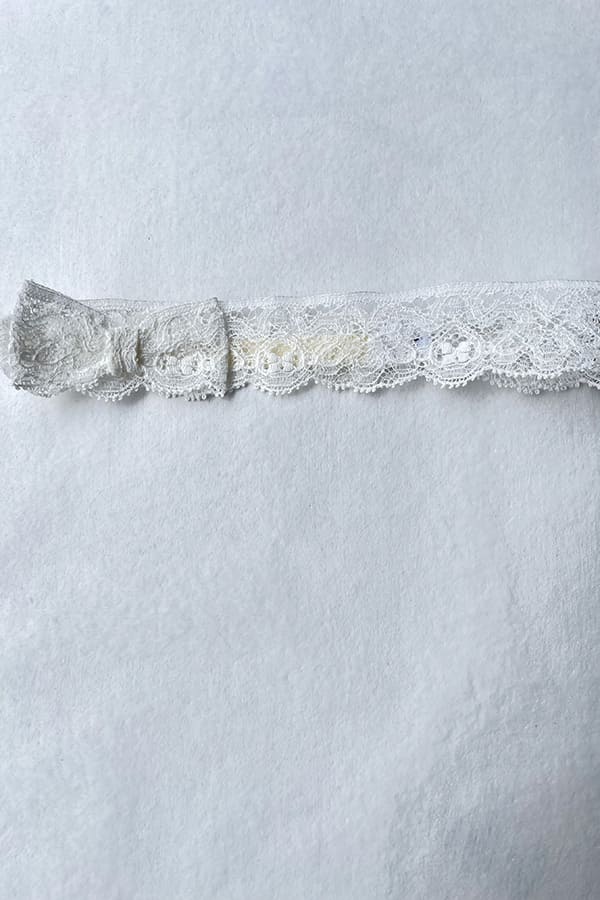 Bandeau cheveux bébé fille en dentelle blanc cassé avec nœud sur le côté. A porter pour un baptême ou une cérémonie. Photo du bandeau à plat.