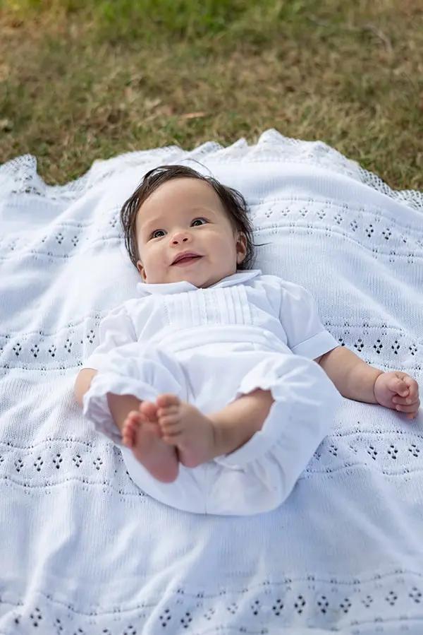 Barboteuse Baptême bébé garçon Augustin en piqué de coton blanc et dentelle de coton. Création française Fil de Légende. Photo de la barboteuse portée par un bébé allongé.