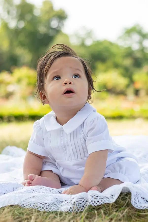 Barboteuse Baptême bébé garçon Augustin en piqué de coton blanc et dentelle de coton. Création française Fil de Légende. Photo d'un bébé garçon portant la barboteuse.