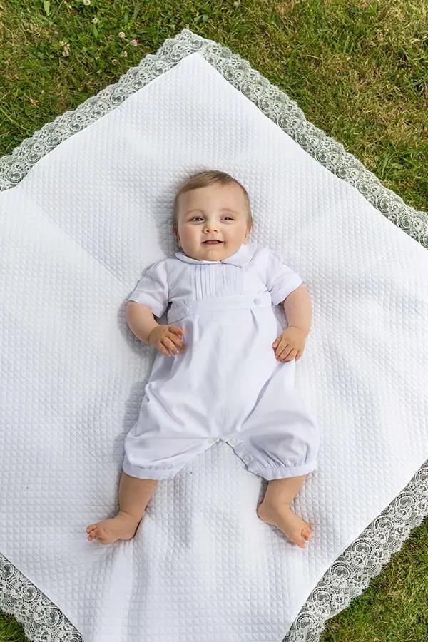 Barboteuse Baptême bébé garçon Augustin en piqué de coton blanc et dentelle de coton. Création française Fil de Légende. Photo de la barboteuse portée par un bébé.