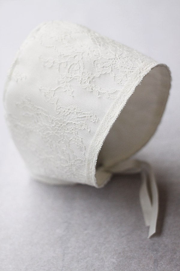 Bonnet de baptême bébé fille Aurélia en dentelle italienne blanc cassé doublé coton. Création française Fil de Légende.  Photo du bonnet vu de côté.