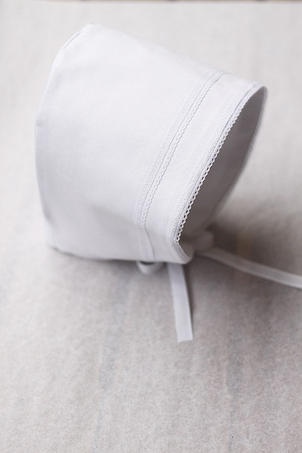 Bonnet de baptême bébé garçon Léo en coton blanc et galons de dentelle de coton. Création française Fil de Légende. Photo du bonnet vu de côté.