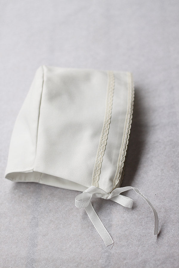 Bonnet de baptême bébé garçon Oscar en coton blanc cassé et dentelle de coton ivoire. Création française Fil de Légende. Photo du bonnet vu de côté.