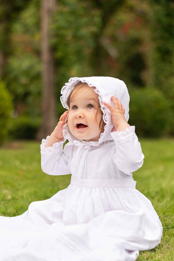 Bonnet baptême bébé fille Marie en coton blanc et dentelle de Calais. Création française Fil de Légende. Photo du bonnet porté par une petite fille vue de loin.