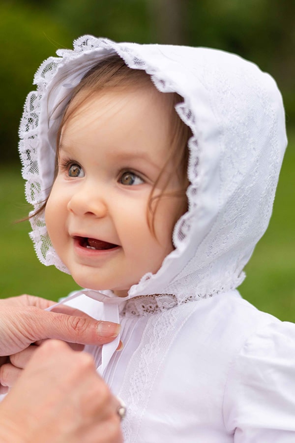 Bonnet baptême bébé fille Marie en coton blanc et dentelle de Calais. Création française Fil de Légende. Photo du bonnet porté par une petite fille.