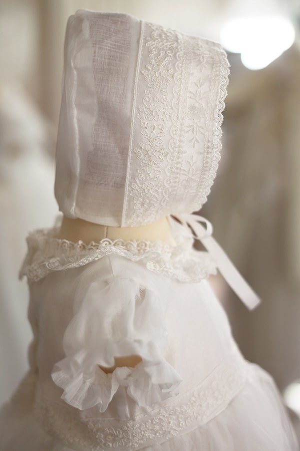 Bonnet de baptême bébé fille Gloria en mousseline et dentelle blanc cassé. Création française Fil de Légende. Disponible en ligne et en boutique à Neuilly-sur-Seine.