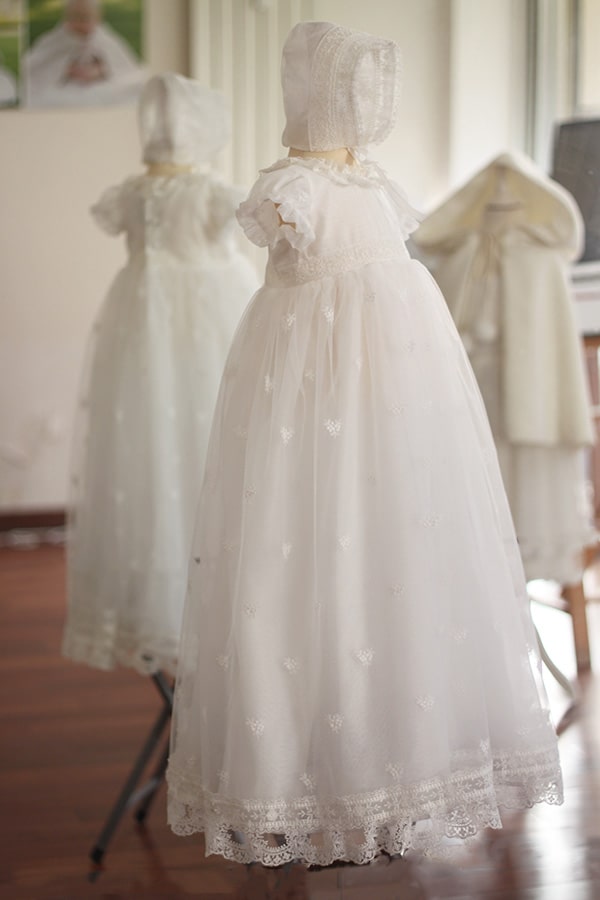 Bonnet de baptême bébé fille Gloria en mousseline et dentelle blanc cassé. Création française Fil de Légende. Photo du bonnet porté avec la robe Gloria.