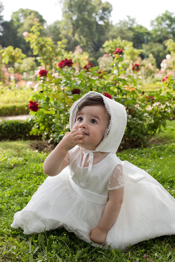 Bonnet de baptême bébé fille Maya en satin italien blanc cassé et dentelle française de calais Caudry. Création française Fil de Légende. Photo du bonnet porté par une petite fille.