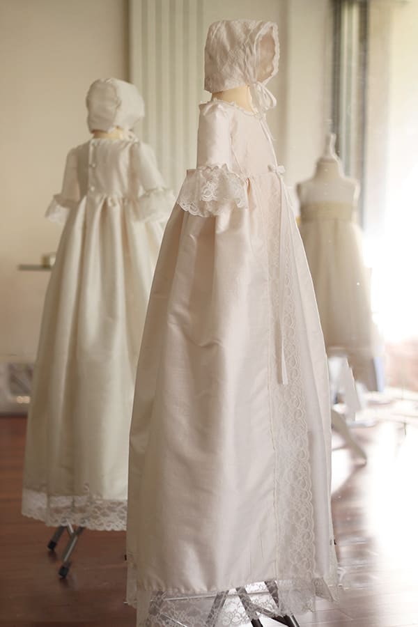 Bonnet de baptême pour bébé fille en soie et dentelle blanc cassé. Photo du bonnet porté avec la robe longue de baptême traditionnelle assortie.