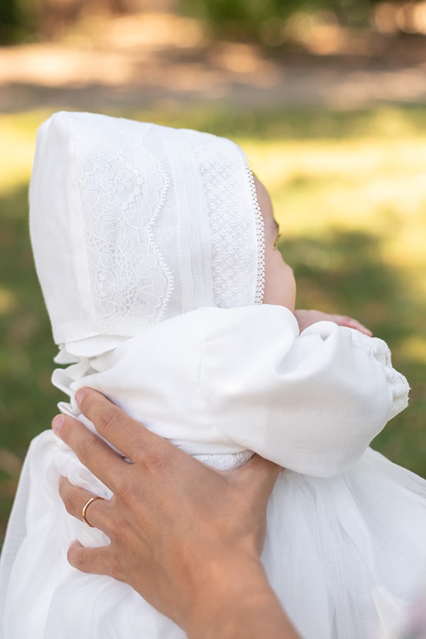 Bonnet baptême bébé en mousseline et dentelle blanc cassé. Modèle Augustine. Création française Fil de Légende. Photo du bonnet porté par un bébé fille.