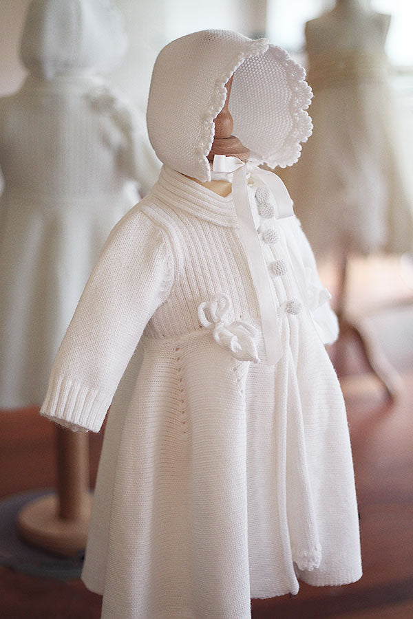 Bonnet de baptême Pauline tricoté en laine mélangée blanc cassé. Bordures de bonnet faites au crochet à la main. Création française Fil de Légende. Photo du bonnet porté avec le manteau assorti.
