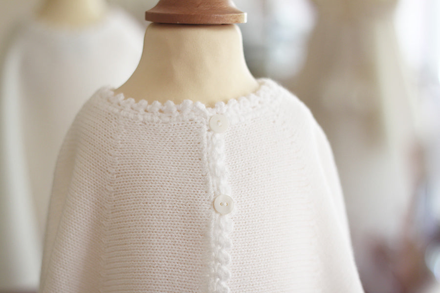 Cape de baptême en maille tricotée blanche avec une bordure festonnée faite au crochet à la main. Création française Fil de Légende. Photo de l'encolure de la cape.