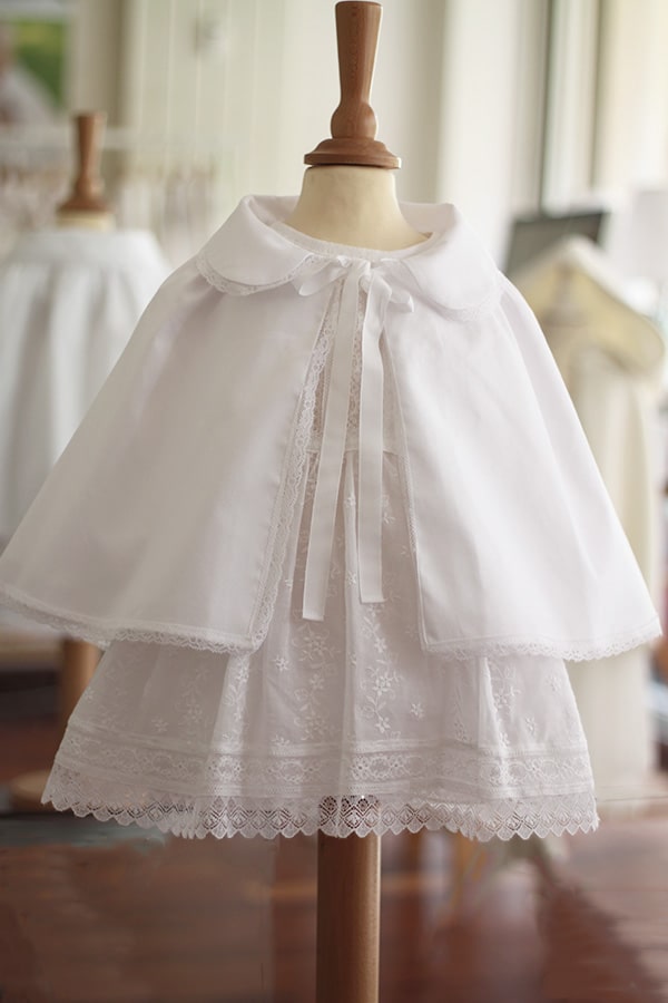 Cape de baptême bébé fille en coton blanc et galon de dentelle. Création française Fil de Légende. Photo de la cape portée avec une robe de baptême sur mannequin de couture.