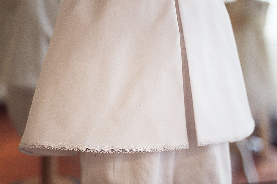Cape de baptême bébé garçon Adrien en coton blanc et dentelle de coton.  Création française Fil de Légende. Photo du galon de dentelle en bas de la cape.