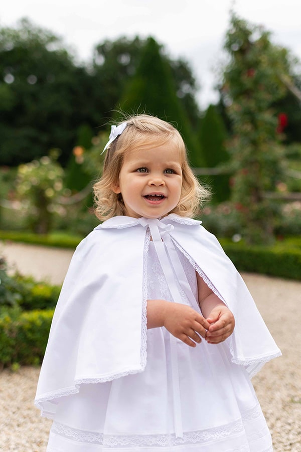 Cape de baptême bébé fille en coton blanc et galon de dentelle. Création française Fil de Légende. Photo de la cape portée par une petite fille.
