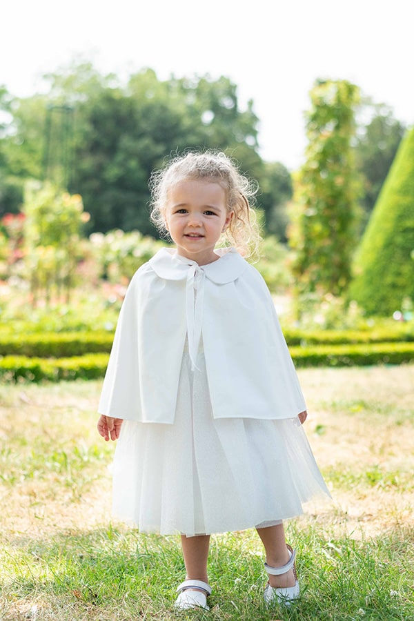 Cape de baptême bébé en coton blanc cassé. Création française Fil de Légende.  Photo de la cape portée par-dessus une robe de cérémonie fille.