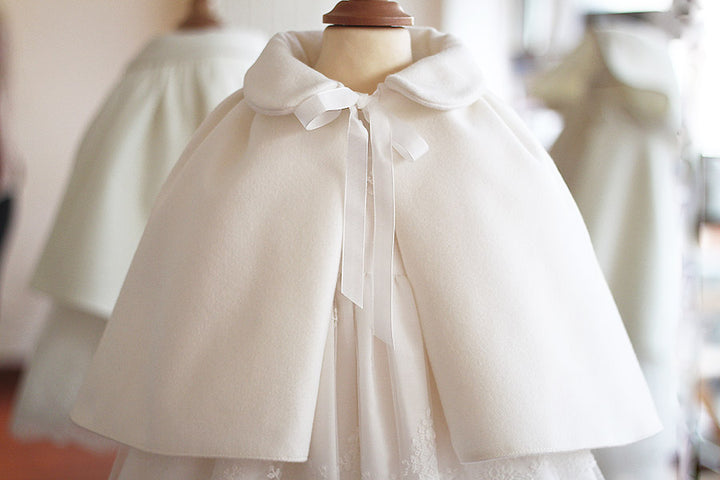 Cape de baptême fille pour l'automne hiver en lainage blanc cassé doublée polaire. Création française Fil de Légende. Photo du gros plan de la cape. 