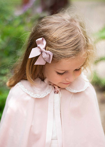 Pince cheveux noeud en gros grain de couleur vieux rose. Parfait pour sublimer une coiffure de petite fille à l'occasion d'une cérémonie. Photo de la barrette portée avec une cape de cérémonie rose.