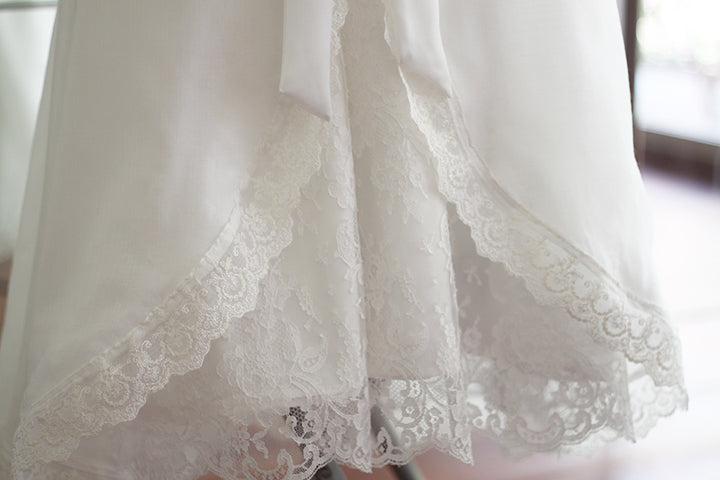 Cape de baptême longue traditionnelle pour baptême en mousseline blanc cassé et dentelle fine. Se ferme avec un large ruban. Fait main en France. Gros plan sur les dentelles.