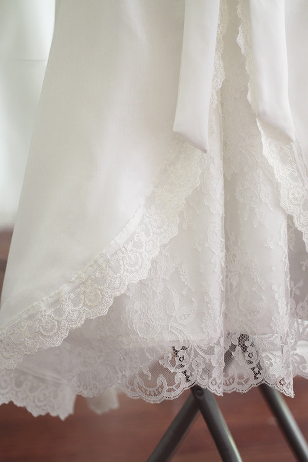 Cape de baptême longue traditionnelle pour baptême en mousseline blanc cassé et dentelle fine. Se ferme avec un large ruban. Fait main en France. Gros plan sur dentelle.