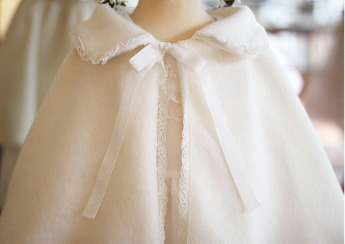 Cape d'hiver bébé fille pour cérémonie  ou baptême en lainage blanc cassé et bordure dentelle. Gros plan