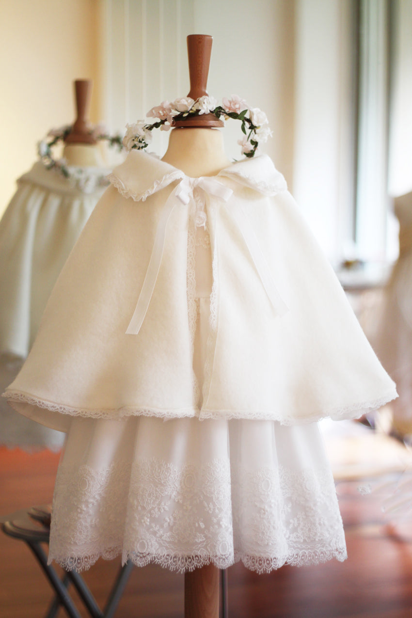 Cape d'hiver bébé fille pour cérémonie  ou baptême en lainage blanc cassé et bordure dentelle. Magasin Fil de Légende Paris, Neuilly-sur-Seine.