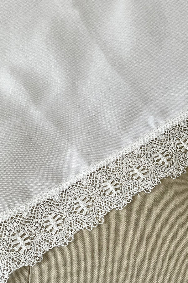 Châle de baptême bébé en coton blanc bordé d'un large galon de dentelle de coton.  Gros plan de la dentelle.