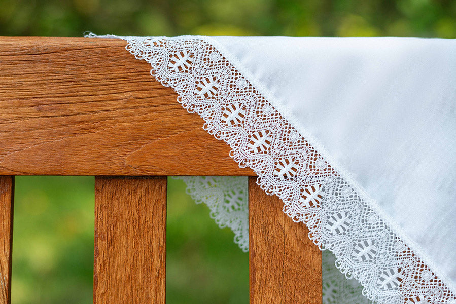 Châle de baptême bébé en coton blanc bordé d'un large galon de dentelle de coton. Photo de la dentelle à la lumière naturelle.
