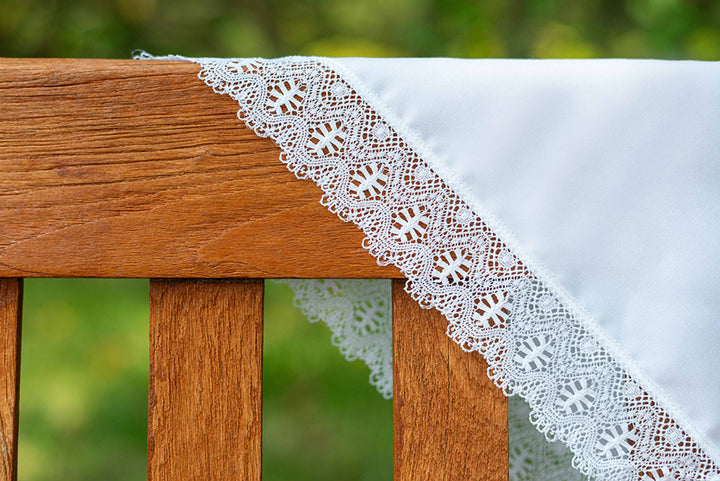 Châle de baptême bébé en coton blanc bordé d'un large galon de dentelle de coton. Photo de la dentelle à la lumière naturelle.