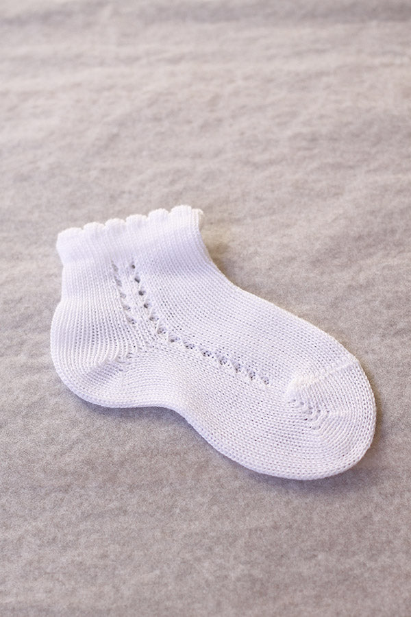 Chaussettes bébé garçon en coton blanc ajouré avec un bord dentelé. Parfaites pour être portées avec une tenue de cérémonie pour bébés.