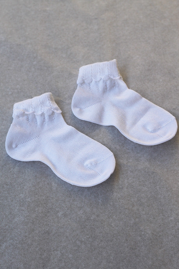 Chaussettes bébé fille en coton blanc avec un revers dentelé. Parfaites pour êtres portées avec une robe blanche de cérémonie pour bébé ou une robe de baptême.