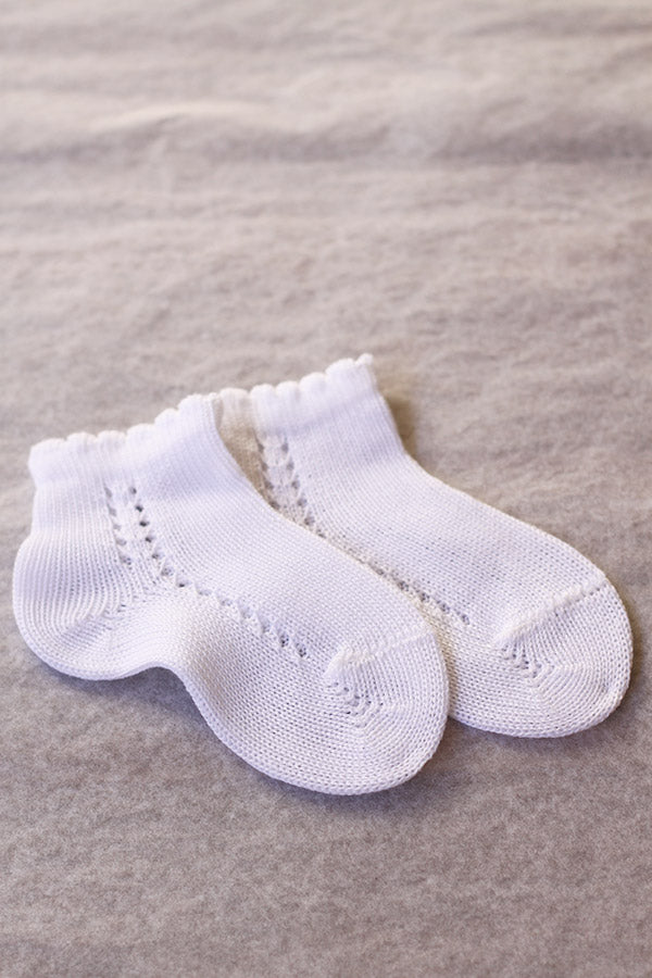 Chaussettes bébé garçon en coton blanc ajouré avec un bord dentelé. Parfaites pour être portées avec une tenue de cérémonie pour bébés.