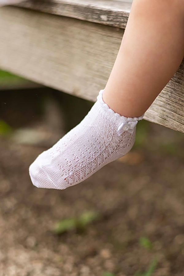 Chaussettes bébé fille en coton blanc ajourées avec un bord dentelé et un nœud en satin blanc sur le côté. A porter avec une robe de cérémonie bébé ou une robe de baptême - vue détaillée