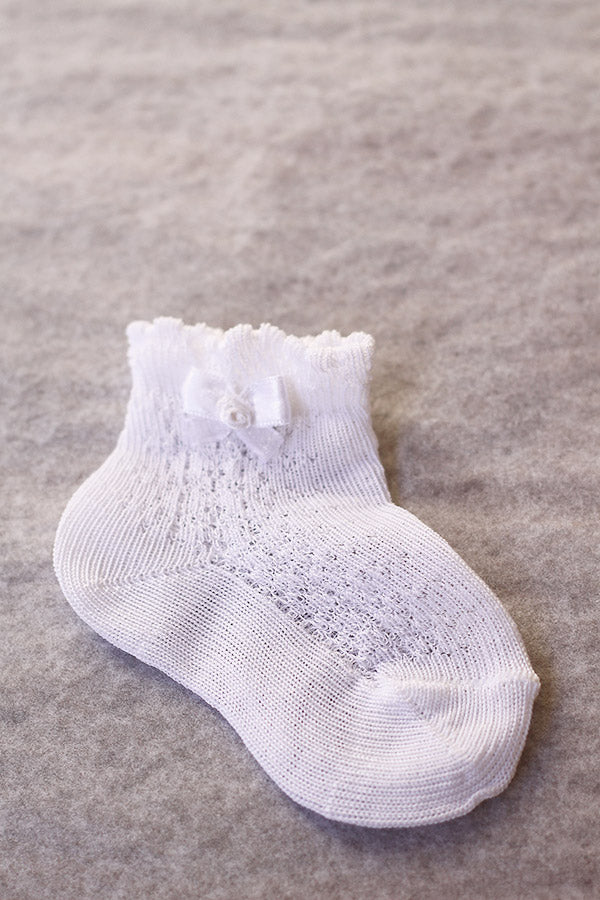 Chaussettes bébé fille en coton blanc ajourées avec un bord dentelé et un noeud en satin blanc sur le côté. A porter avec une robe de cérémonie bébé ou une robe de baptême - Fil de Légende Paris, Neuilly-sur-Seine