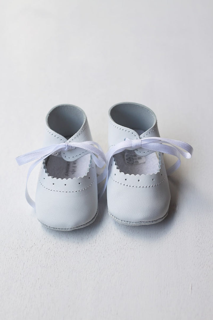 Chaussons ballerines bébé fille en cuir blanc pour cérémonie ou baptême. Se ferme en nouant un ruban de satin. Vue de face.