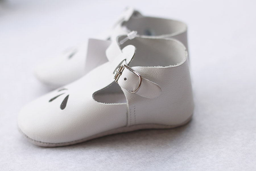 Chaussons cérémonie baptême bébé en cuir blanc. Idéal pour la saison printemps/ été. Ouverture à boucle. Gros plan sur chaussons.