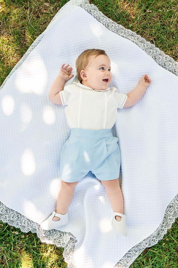 Chaussons baptême cérémonie bébé fille ou garçon pour l'été. Chaussons en cuir blanc avec une ouverture à boucle. Photo des chaussons portés avec ensemble bleu et blanc.
