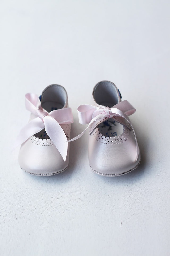 Ballerines bébé fille en cuir rose pâle avec une bordure dentelée pour cérémonie ou fête. Les chaussons se ferment avec un noeud en satin rose à nouer. Vue éloignée. 