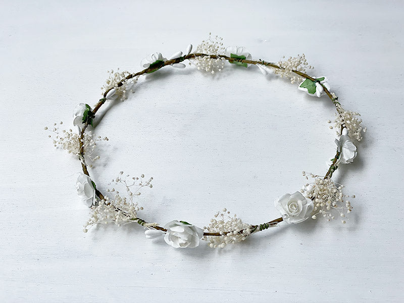 Couronne artificielle de petites fleurs blanches et gypsophile à porter avec une robe de cérémonie pour enfants. Parfait pour sublimer une coiffure de petite fille. Photo de la couronne posée à plat.
