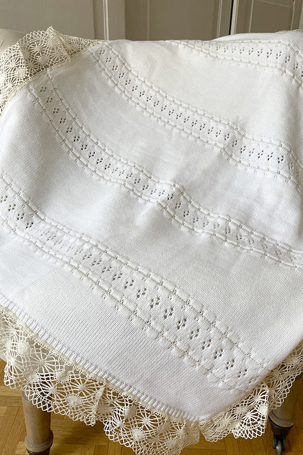Couverture bébé pour cérémonie ou baptême en lainage blanc cassé, avec motifs ajourés et large galon de dentelle. Magasin Fil de Légende Paris, Neuilly-sur-Seine.