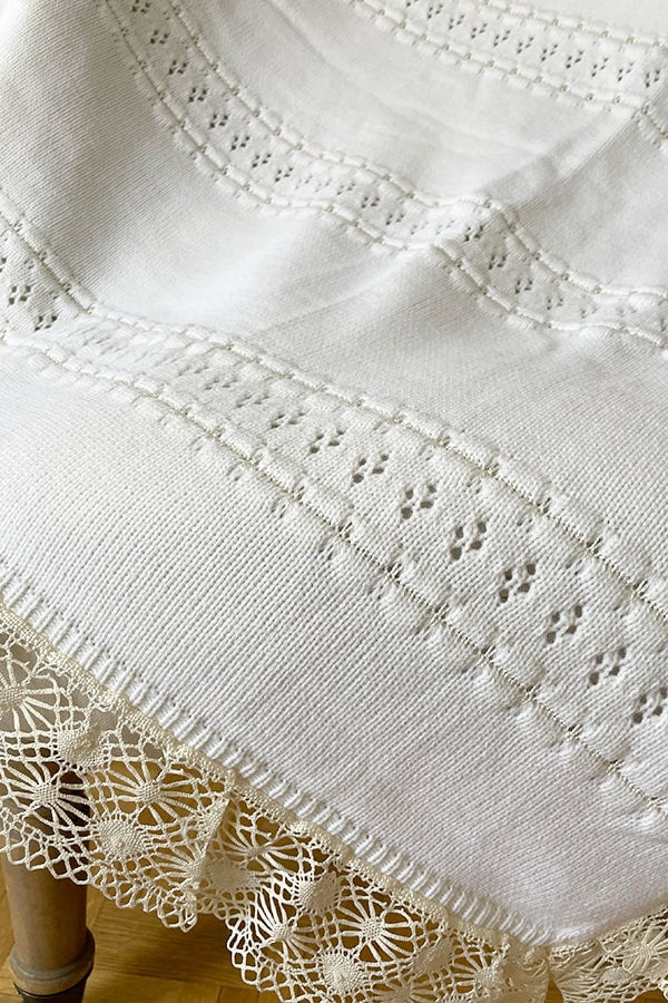 Couverture bébé pour cérémonie ou baptême en lainage blanc cassé, avec motifs ajourés et large galon de dentelle. Gros plan sur motifs ajourés.