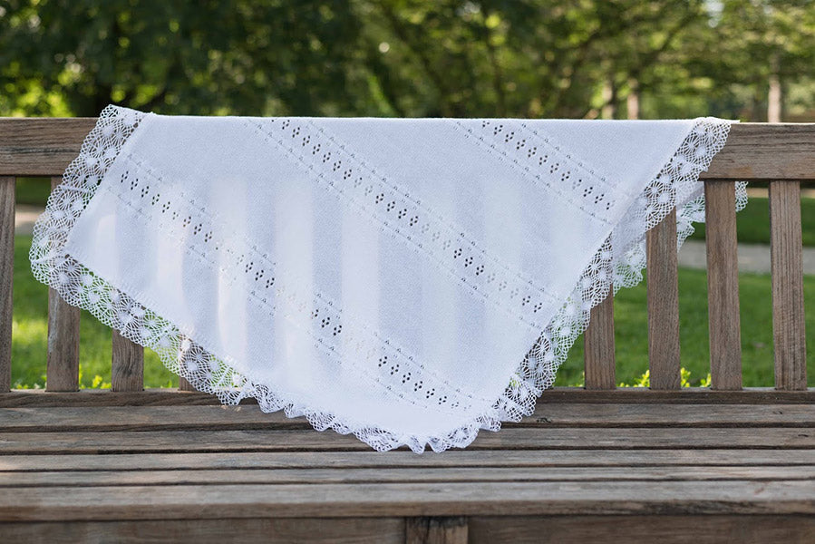 Couverture tricotée pour bébé en coton ajouré, bordée d'un large galon de dentelle de coton. Idéal pour baptême. Photo vue de loin.